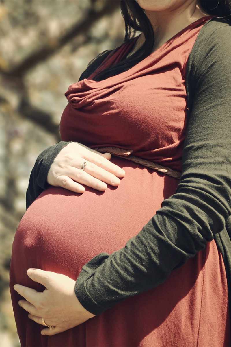 Een staande zwangrere vrouw met haar handen rond haar buik
