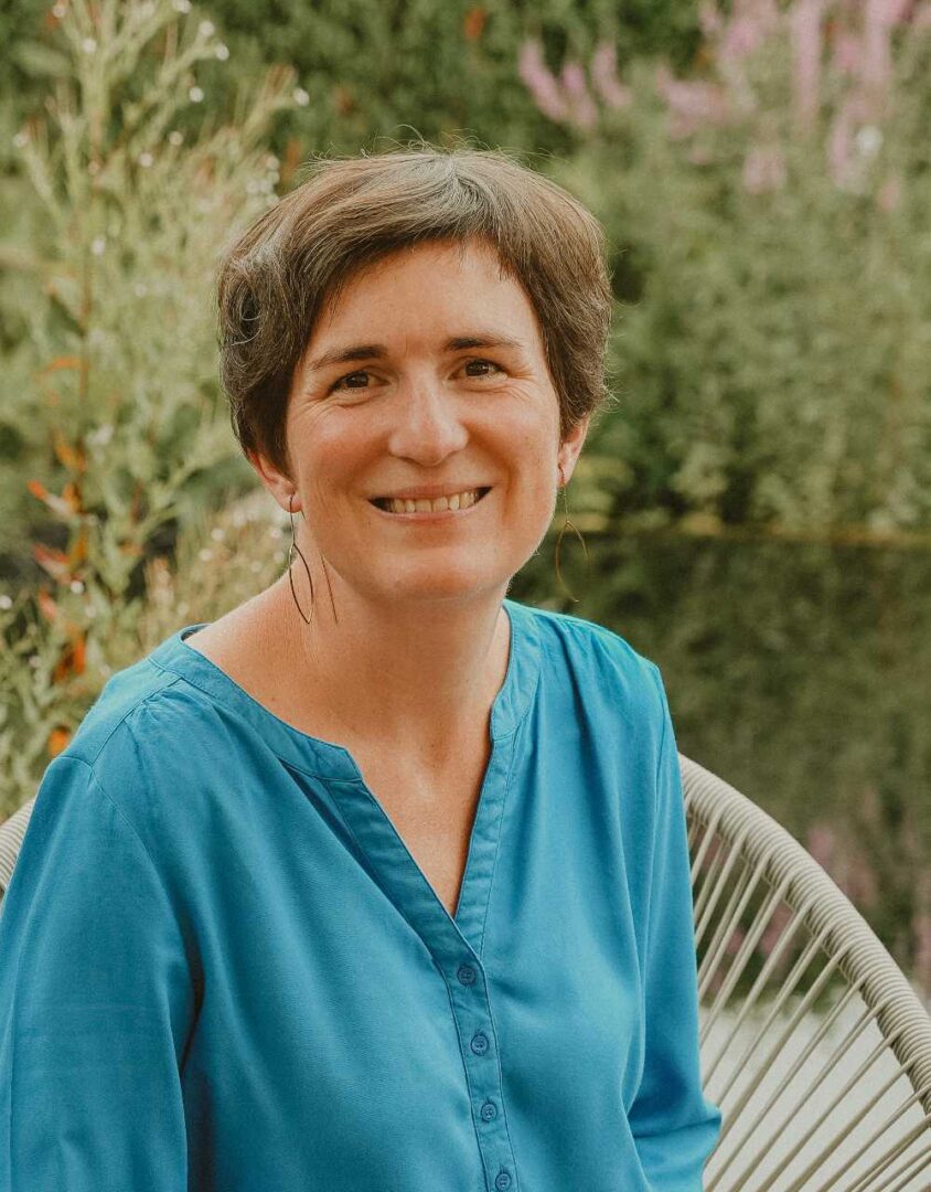 Portret van Hanne De Meyer in haar tuin met een blauwe blouse aan